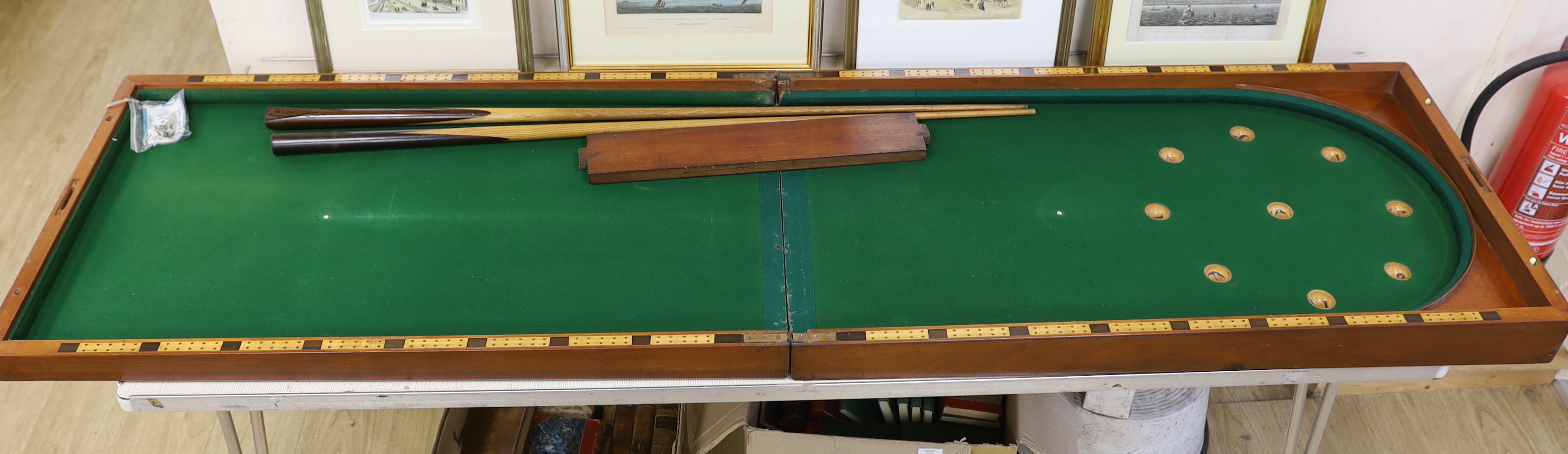 A Victorian folding cased bagatelle board, green baize interior with markers and two cues, 223.5cm open
